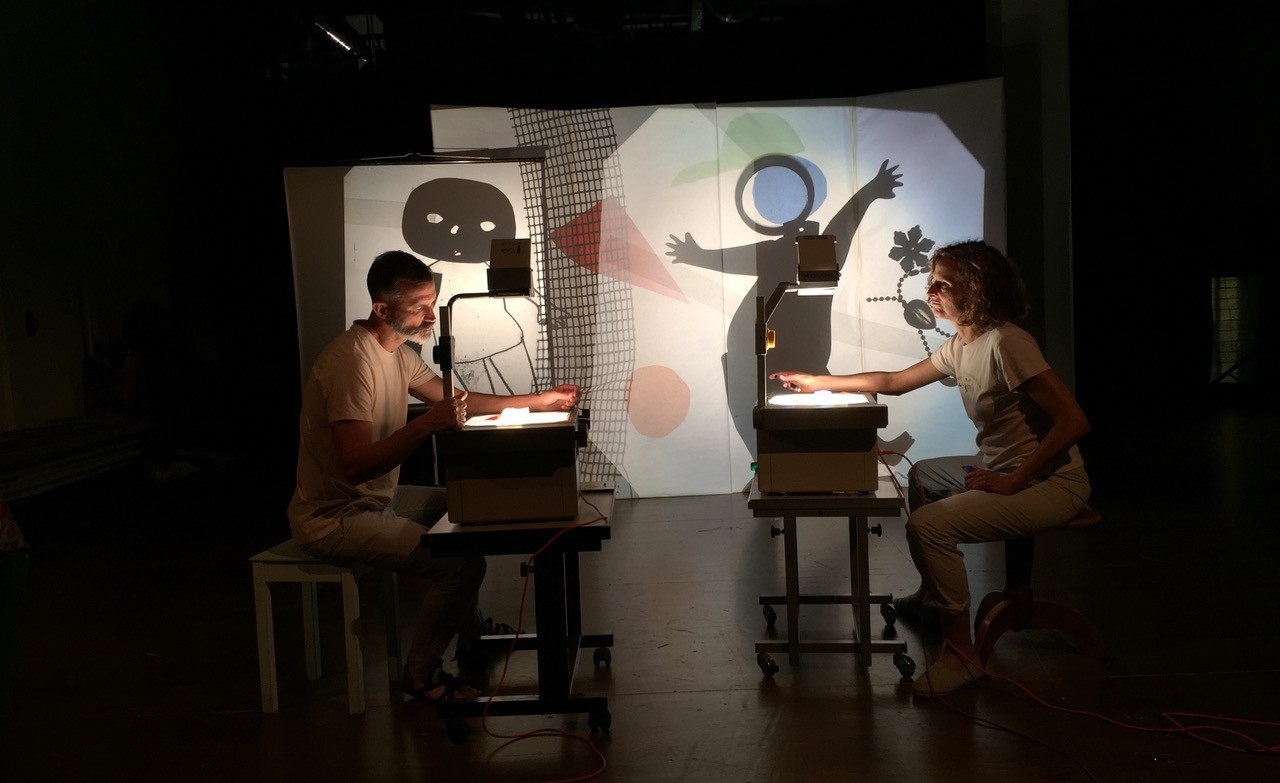 Szenenbild aus dem Theaterstück. Zwei Erwachsene malen eine Figur.