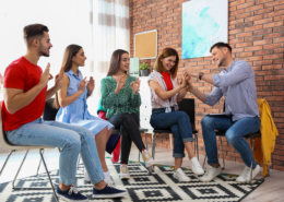 Gebärdensprachkurs mit vier Teilnehmenden und einem jungen Lehrer, der einer Teilnehmerin eine Handgebärde korrigiert.