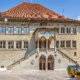 Berner Rathaus von vorne fotografiert. Auf dem Rathausplatz stehen Pflanzenkübel, Tische und Stühle von der Rathausbar.