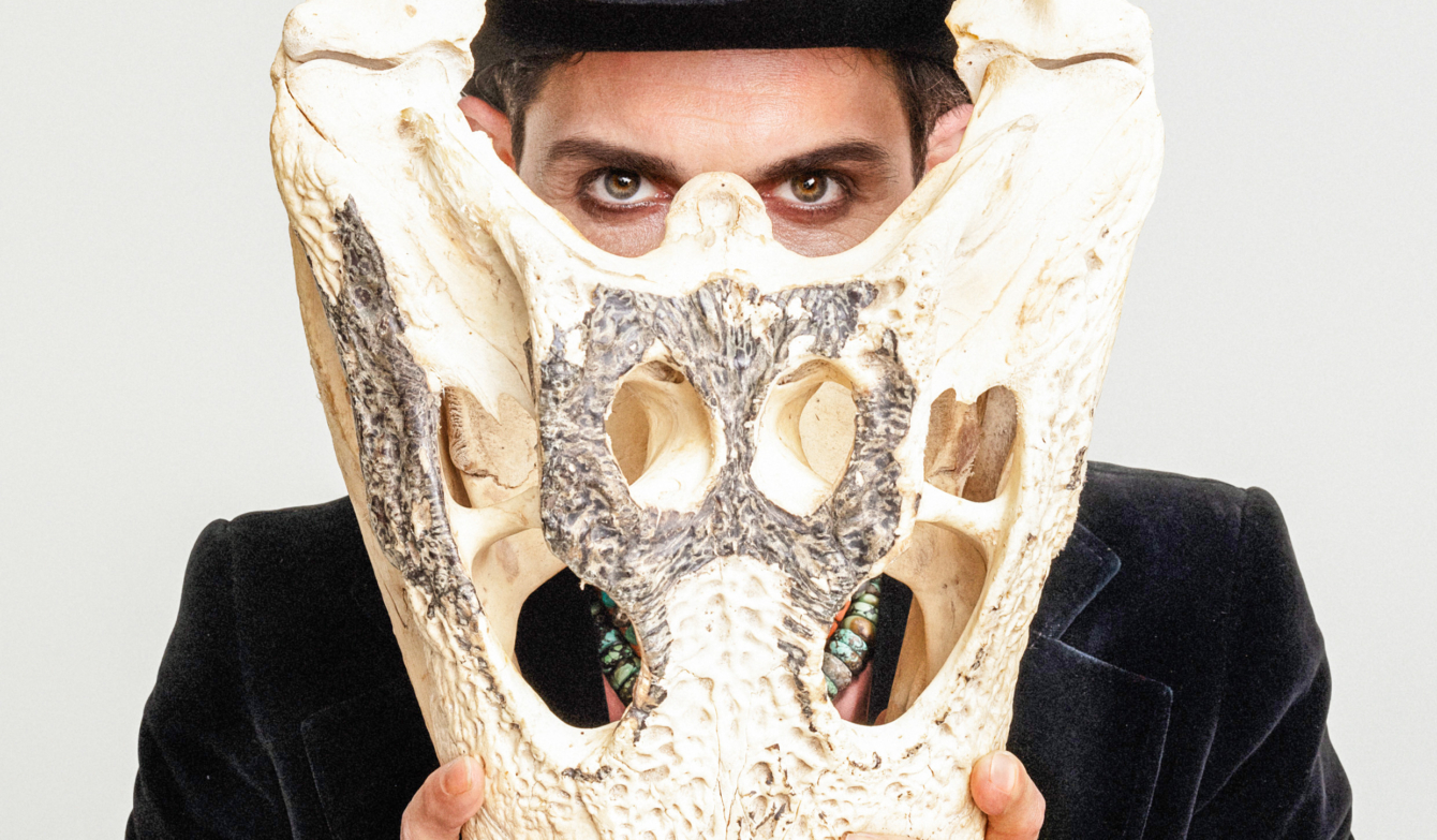 Visualbild Darsteller von Frank Buchser im Anzug und mit Hut, vor sich ein Büffel-Schädelknochen haltend.