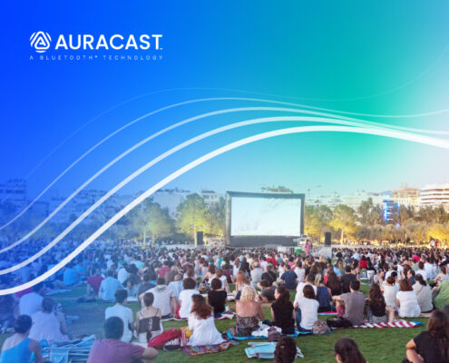 Menschen sitzen bei einer Open-Air-Filmvorführung auf einer Wiese. Über dem Bild liegt ein blau-grüner Auracast-Verlauf mit geschwungenen Linien und dem Auracast-Logo.