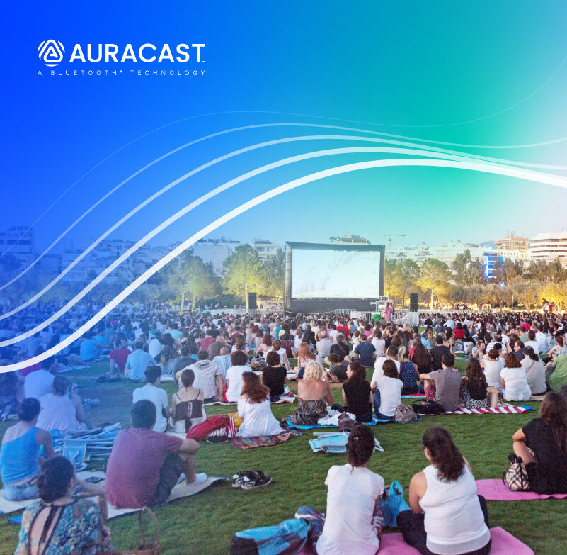Menschen sitzen bei einer Open-Air-Filmvorführung auf einer Wiese. Über dem Bild liegt ein blau-grüner Auracast-Verlauf mit geschwungenen Linien und dem Auracast-Logo.